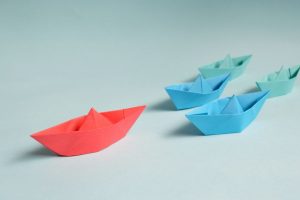 red-paper-boat-leading-smaller-blue-paper-boats