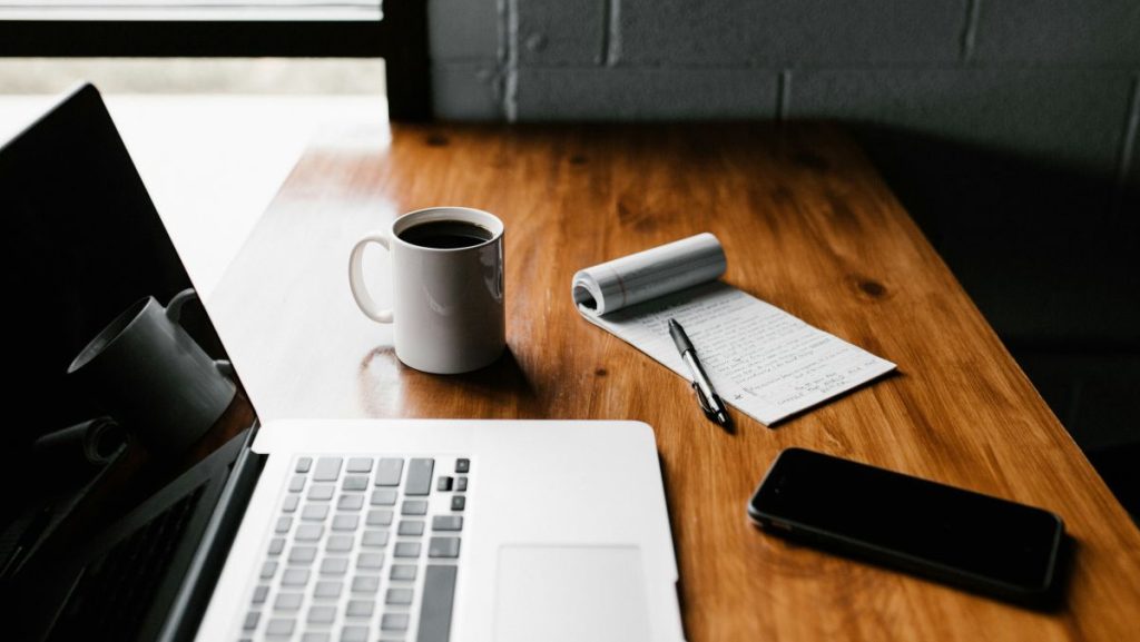laptop open next to mug and notebook