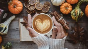 hands holiding latte csourrounded by leaves and pumpkins